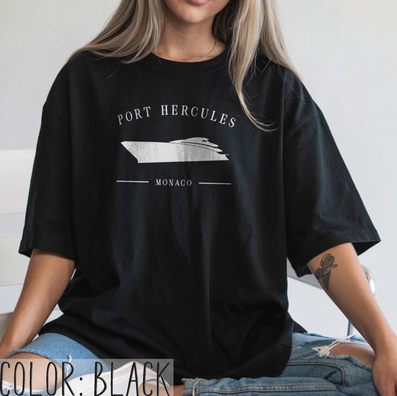 May include: Black t-shirt with a white graphic of a yacht and the text "PORT HERCULES MONACO". The shirt is a casual style, suitable for everyday wear.