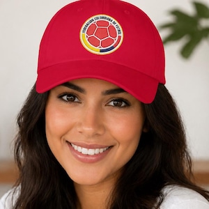 Puede incluir: Gorra de b&eacute;isbol roja con el emblema de la Federaci&oacute;n Colombiana de F&uacute;tbol. El emblema presenta un dise&ntilde;o de bal&oacute;n de f&uacute;tbol con detalles amarillos, azules y rojos. La gorra tiene un dise&ntilde;o cl&aacute;sico de seis paneles.