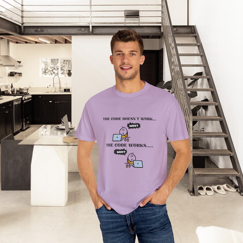 May include: A light purple t-shirt with the text "THE CODE DOESN'T WORK... WHY? THE CODE WORKS..... WHY?" and a cartoon graphic of a person working on a laptop. The shirt is made of a soft material.