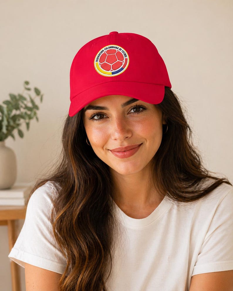 Puede incluir: Gorra de b&eacute;isbol roja con el emblema de la Federaci&oacute;n Colombiana de F&uacute;tbol. La gorra tiene una visera curva y un logotipo circular con un dise&ntilde;o de bal&oacute;n de f&uacute;tbol. La persona lleva una camiseta blanca.