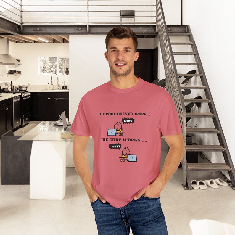 May include: A dusty rose t-shirt with the text "THE CODE DOESN'T WORK... WHY? THE CODE WORKS..... WHY?" and a cartoon graphic of a person at a laptop. The shirt is being worn by a person in blue jeans.