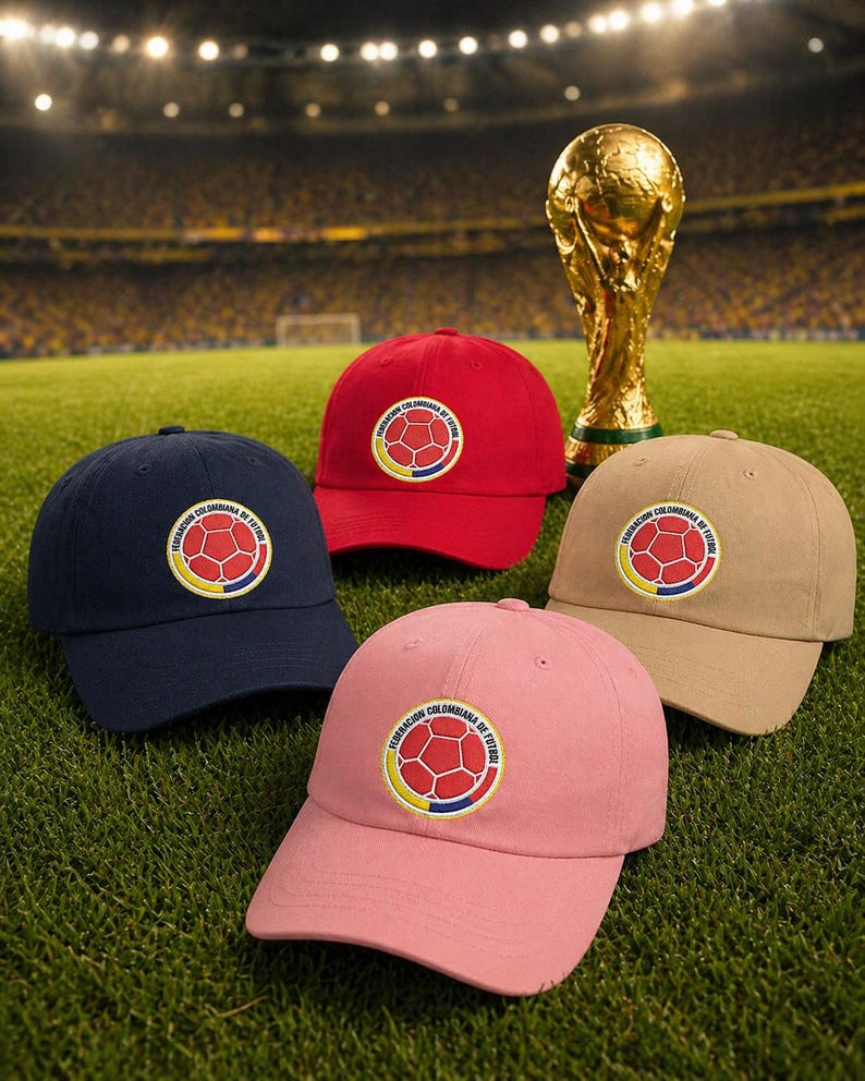 Puede incluir: Cuatro gorras de b&eacute;isbol en azul marino, rojo, beige y rosa, cada una con un emblema circular con un dise&ntilde;o de bal&oacute;n de f&uacute;tbol y texto. Un trofeo dorado est&aacute; en el fondo, sobre un campo verde.