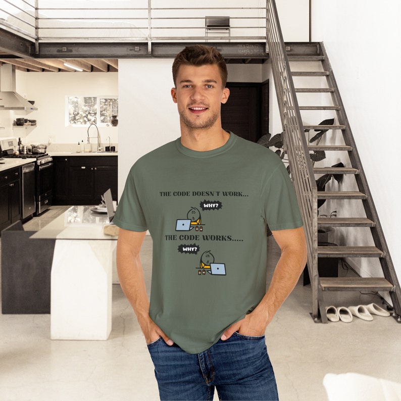 May include: Olive green t-shirt with the text "THE CODE DOESN'T WORK... WHY? THE CODE WORKS..... WHY?" and a cartoon graphic of a stick figure working on a laptop. The shirt is made of a soft material.