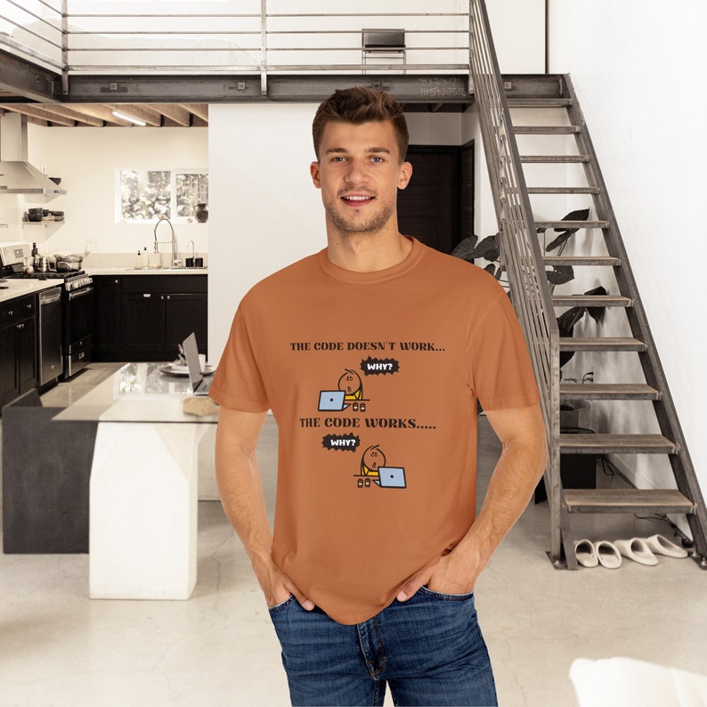 May include: A rust-colored t-shirt with the text "THE CODE DOESN'T WORK... WHY? THE CODE WORKS..... WHY?" and a cartoon graphic of a person at a laptop. The person is wearing blue jeans.