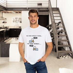 May include: White t-shirt with the text "THE CODE DOESN'T WORK... WHY? THE CODE WORKS..... WHY?" and a cartoon graphic of a person working on a laptop. The shirt is worn by a person.