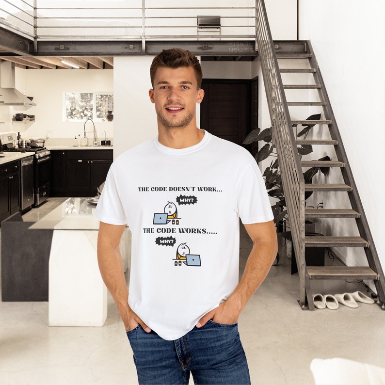 May include: White t-shirt with the text "THE CODE DOESN'T WORK... WHY? THE CODE WORKS..... WHY?" and a cartoon graphic of a person working on a laptop. The shirt is worn by a person.