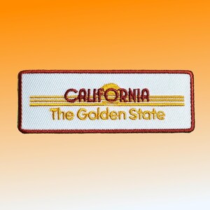 May include: White embroidered patch with red border. The patch features a yellow sun with a red outline and the text "CALIFORNIA" in red. Below the sun is the text "The Golden State" in yellow.