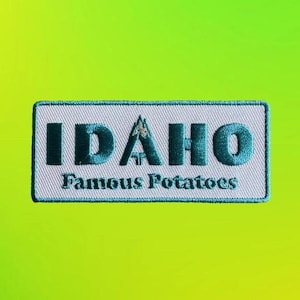 May include: Embroidered patch with the word "IDAHO" in teal letters above "Famous Potatoes" on a white rectangular background. The patch has a teal border and a mountain graphic in the "A". The background is a gradient of green and yellow.
