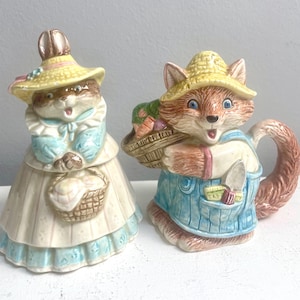 May include: A ceramic salt and pepper shaker set featuring a rabbit and a fox. The rabbit is wearing a straw hat and a blue dress, and is holding a basket of eggs. The fox is wearing a straw hat and overalls, and is holding a basket of vegetables.