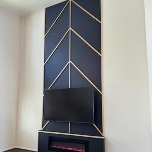 May include: A navy blue wall panel with a geometric design, gold trim, and a mounted television. Below the TV is a black fireplace with a red glowing flame effect. The panel is mounted on a white wall.