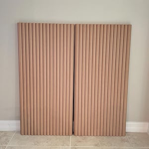 May include: Two wooden panels with vertical, rounded slats. The panels are a light brown color and are positioned side-by-side. The background is a neutral wall and tiled floor.