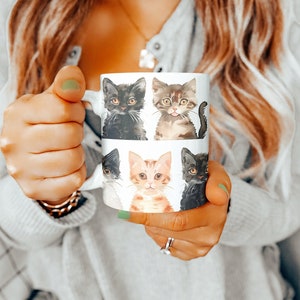 Puede incluir: Taza de cerámica blanca con un diseño de cuatro gatitos. Los gatitos están en un patrón de cuadrícula y cada uno tiene una expresión diferente. La taza está siendo sostenida por una mano.