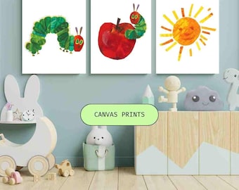May include: Three canvas prints featuring illustrations. One shows a green caterpillar, another a red apple with a caterpillar, and the third a yellow sun. The prints are displayed on a light blue wall above a wooden cabinet. The text "CANVAS PRINTS" is visible.