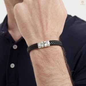 May include: A black leather braided bracelet with silver beads. The beads are engraved with the names "Hiram", "Sarah", and a footprint symbol.