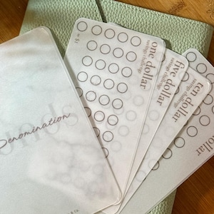 May include: A light green leather wallet with savings challenge cards. The cards are labelled with denominations from one to twenty pounds and feature circles for tracking savings. The word "Denomination" is printed on the front.