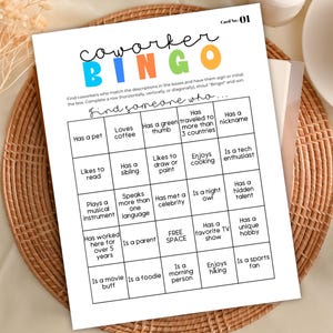 Puede incluir: Una tarjeta de juego de bingo para compañeros de trabajo con una cuadrícula de descripciones como "Ama el café" y "Tiene una mascota". La tarjeta es blanca con texto colorido y está sobre un mantel individual tejido.
