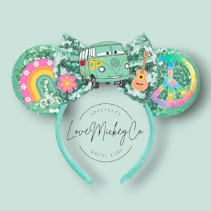 May include: Mint green sequined headband with mouse ears featuring a central bow. The left ear displays a rainbow and flower, while the right ear shows a peace sign. The bow features a cartoon van, a guitar, and a flower. Text reads Love Mickey Co.