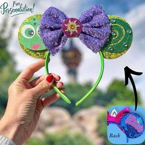 May include: Green and purple glitter mouse ears with a green and yellow swirl design on one ear and a purple bow with a yellow sun design in the center. The headband is green. The back of the ears are blue with glitter and the text "Back" is written in white.