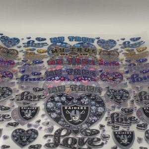 Puede incluir: Hoja transparente de pegatinas con varios diseños. Incluye formas de corazón, la palabra "Love" y el texto "MY TRUE". Algunas pegatinas presentan el logotipo de los Raiders. Los colores incluyen azul, plata y rosa.