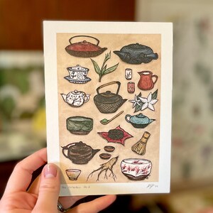 May include: A brown and beige illustration of a tea collection with various teapots, cups, bowls, and other tea-related items. The illustration is titled "Tea Collection No. 2".