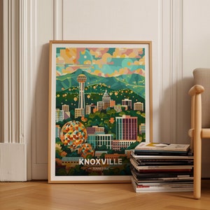 Puede incluir: Una impresión artística enmarcada que presenta una colorida ilustración de Knoxville, Tennessee. La obra de arte muestra el horizonte de la ciudad, incluyendo la Sunsphere y otros puntos de referencia, con el texto "KNOXVILLE - TENNESSEE" en la parte inferior. La impresión está en un marco de madera.
