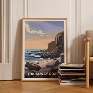 May include: A framed illustration of a rocky coastline with a beach and ocean. The illustration is in a muted color palette of blues, greens, and browns. The text "Causeway Coast" is at the bottom of the illustration.