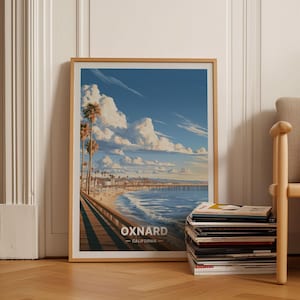 May include: A framed wall art print featuring a coastal scene of Oxnard, California, with a wooden pier, sandy beach, palm trees, and blue ocean under a sky filled with large white clouds. The text reads OXNARD CALIFORNIA.