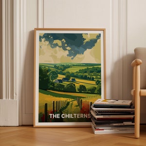 Puede incluir: Un póster enmarcado con una ilustración colorida de una colina verde ondulada con un camino sinuoso que conduce a un pequeño pueblo. El cielo es azul claro con nubes blancas. El póster se titula "THE CHILTERNS".