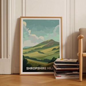 May include: A framed print of a green and blue landscape with a hill in the background. The print has the text "SHROPSHIRE HILL" at the bottom.