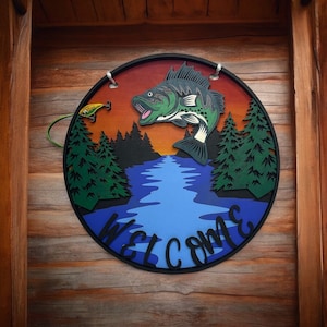 May include: A round wooden sign with a welcome message and a graphic of a fish jumping out of the water. The sign has a blue and green color scheme with a sunset background.