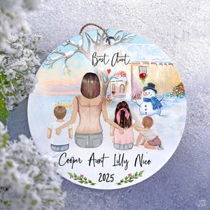 Könnte beinhalten: Runder, personalisierter Weihnachtsschmuck mit einer Familienszene mit einer Frau und drei Kindern in einer Winterlandschaft. Der Schmuck trägt den Text "Best Aunt", Namen und das Jahr 2025. Ein Schneemann ist ebenfalls abgebildet.