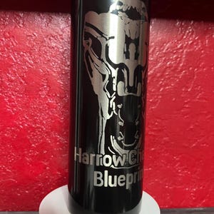 Peut inclure: Un gobelet en acier inoxydable noir avec une image gravée en argent d'un crâne et le texte "Harrow: Chapter One Blueprint".