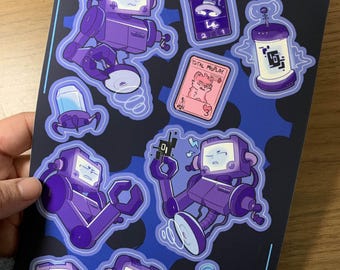 Può includere: Un set di otto adesivi con robot viola e blu con diverse espressioni. Gli adesivi sono su uno sfondo nero con un indirizzo di sito web bianco, "DETERMINUTION.TUMBLR.COM".