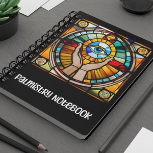 May include: Black notebook with a spiral binding and the text "Palmistry Notebook" printed on the front cover. The cover features a colorful stained glass design with an eye in the center.