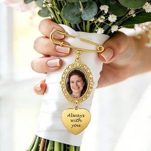 May include: A gold-toned metal brooch pin attached to a white ribbon-wrapped bouquet handle. The pin features an oval frame containing a photograph of a person and a dangling heart-shaped charm engraved with the text Always with you.