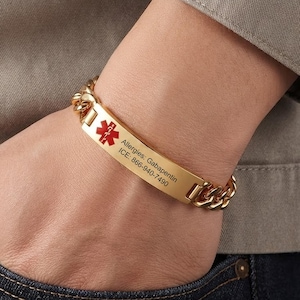 Puede incluir: Una pulsera de alerta médica dorada con una cadena de eslabones y una placa rectangular central. La placa muestra un símbolo rojo de la Estrella de la Vida y el texto grabado: Allergies: Gabapentin, ICE: 866-940-7490.