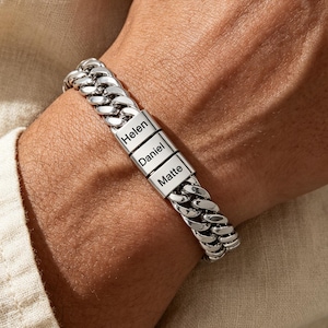 Puede incluir: Una pulsera de cadena tipo barbada en metal plateado con eslabones pulidos entrelazados. La pulsera presenta tres eslabones rectangulares centrales grabados con los nombres Helen, Daniel y Matte, formando una banda continua.