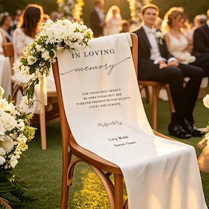 May include: A wooden chair with a white fabric draped over it, adorned with white flowers. The fabric reads "IN LOVING memory" and a message about remembrance. The names Lucy Webb and Daniel Grant are also printed on the fabric. A wedding ceremony is in progress.