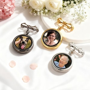 May include: Three personalised photo lockets in gold, silver, and gunmetal finishes. Each locket features a circular photo and a decorative bow-shaped clasp. The lockets are displayed with white flowers and pink rose petals.