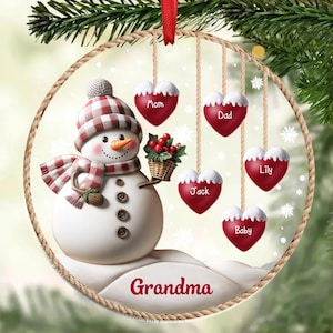May include: A round Christmas ornament featuring a snowman with a plaid hat and scarf, holding a basket of berries. Five heart-shaped ornaments hang below, each with a name. The word "Grandma" is written at the bottom.