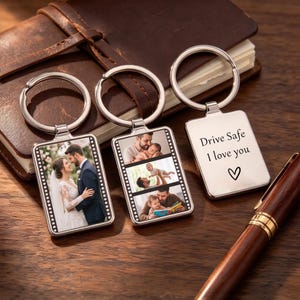 Puede incluir: Tres llaveros rectangulares de metal plateado con anillas. Dos llaveros presentan diseños de tira de película con fotografías de una pareja de novios y un padre con su hijo. Un llavero está grabado con "Drive Safe I love you" y un símbolo de corazón.