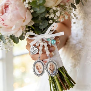 May include: A wedding bouquet charm featuring two oval silver-toned frames with portraits of an older man and woman, white pearl beads, a silver heart charm engraved with the text "you are always in my heart," and a small blue angel wing charm.
