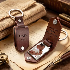 Peut inclure: Deux porte-clés en cuir marron avec des anneaux en métal argenté. L'un est fermé et gravé avec DAD et deux cœurs. L'autre est ouvert, révélant une photo d'une personne tenant un bébé, avec le texte Drive Safe Daddy. We Love you.