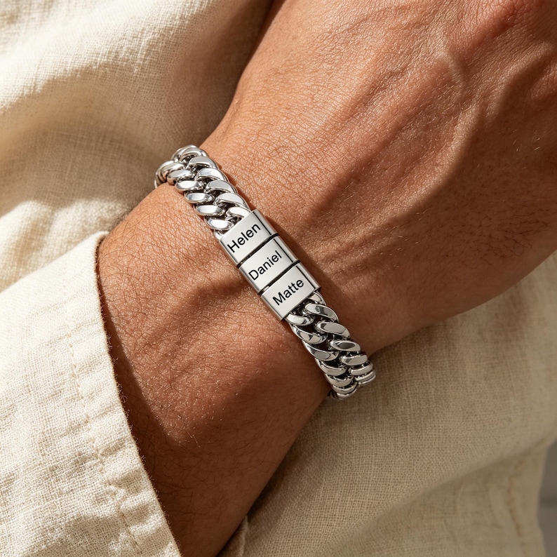 Puede incluir: Una pulsera de cadena tipo barbada en metal plateado con eslabones pulidos entrelazados. La pulsera presenta tres eslabones rectangulares centrales grabados con los nombres Helen, Daniel y Matte, formando una banda continua.
