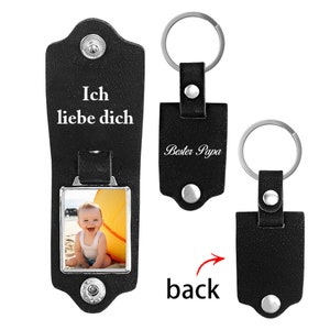 May include: Three black leather keychains with silver metal hardware. One keychain is open, displaying a square photo of a smiling baby and the text Ich liebe dich. Another shows the text Bester Papa. A third shows the back of the keychain.