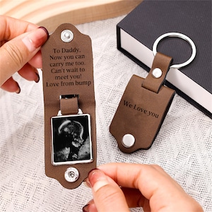 May include: A brown leather keychain with a silver metal ring and snap closures. The interior features a black and white ultrasound image and the text: To Daddy, Now you can carry me too. Can't wait to meet you! Love from bump. The exterior says We Love you.