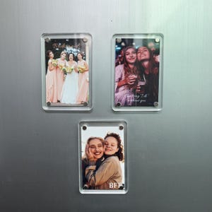 Puede incluir: Tres marcos de fotos magn&eacute;ticos rectangulares de acr&iacute;lico transparente, cada uno con una fotograf&iacute;a diferente. El marco superior izquierdo muestra un grupo de boda con el texto Bridesmaid. El marco superior derecho muestra a dos personas con el texto Can't say I do without you. El marco inferior muestra a dos personas con el texto BFF.