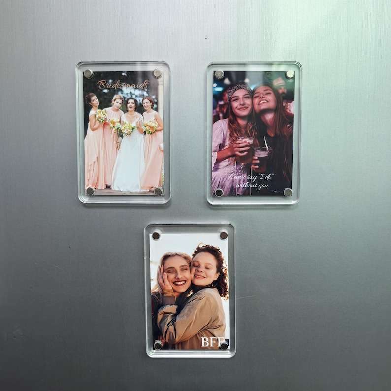 Puede incluir: Tres marcos de fotos magn&eacute;ticos rectangulares de acr&iacute;lico transparente, cada uno con una fotograf&iacute;a diferente. El marco superior izquierdo muestra un grupo de boda con el texto Bridesmaid. El marco superior derecho muestra a dos personas con el texto Can't say I do without you. El marco inferior muestra a dos personas con el texto BFF.