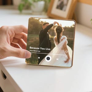 K&ouml;nnte beinhalten: Eine quadratische Acrylplatte mit einem aufgedruckten Foto eines tanzenden Paares im Freien. Das Bild enth&auml;lt eine Musik-Player-Oberfl&auml;che mit dem Text Because You Live und Jesse McCartney sowie Wiedergabesteuerungssymbole.
