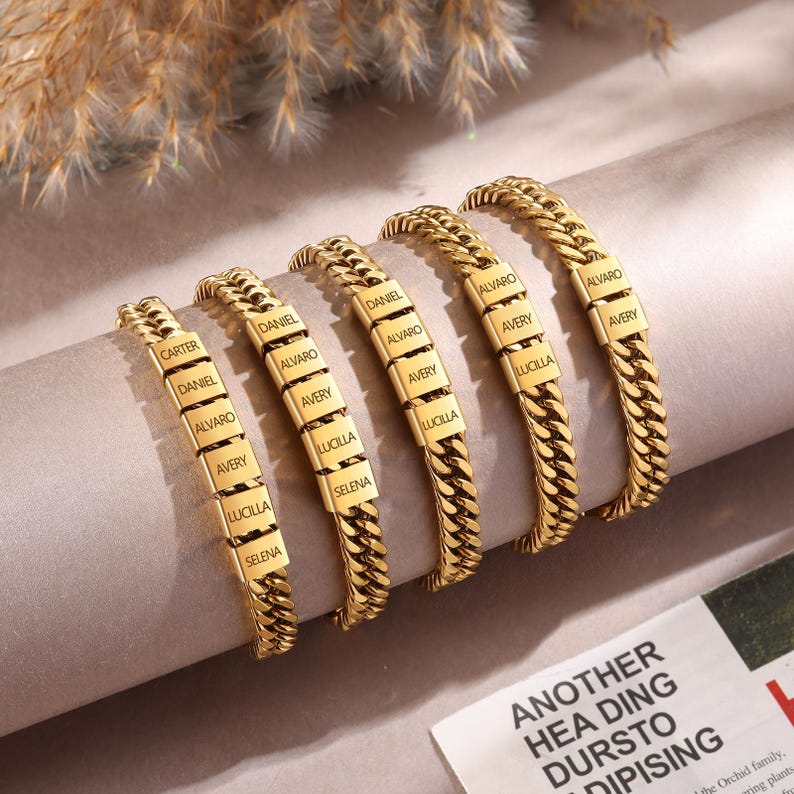 Puede incluir: Cinco pulseras de cadena tipo barbada en tono dorado con eslabones met&aacute;licos rectangulares grabados con varios nombres, incluidos Carter, Daniel, Alvaro, Avery, Lucilla y Selena. Las pulseras est&aacute;n dispuestas en fila, mostrando el acabado met&aacute;lico pulido.